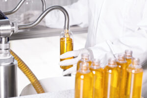 unrecognizable factory worker in white gown and rubber gloves holding plastic bottle and filling it with thick yellow substance from tube. manufacturing of cosmetics or pharmaceutical products