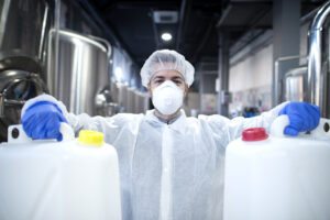 industrial worker with protective mask and white uniform holding plastic cans for chemical industry.
