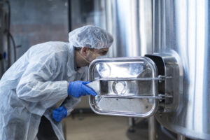 technologist in white suit looking inside machine in food factory production line.